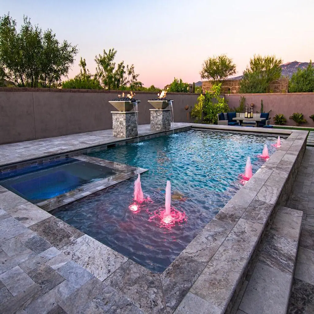 Travertine pool deck with pink-lit fountain jets at dusk