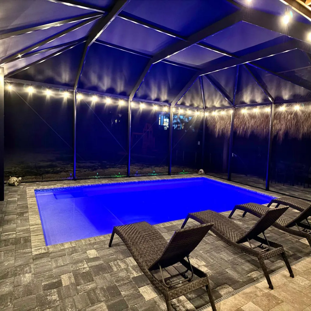 Blue LED-lit pool under a screened lanai at night